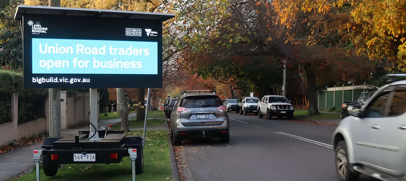 MOBO SAT-3 solar advertising trailer displaying public messaging on a tree-lined street